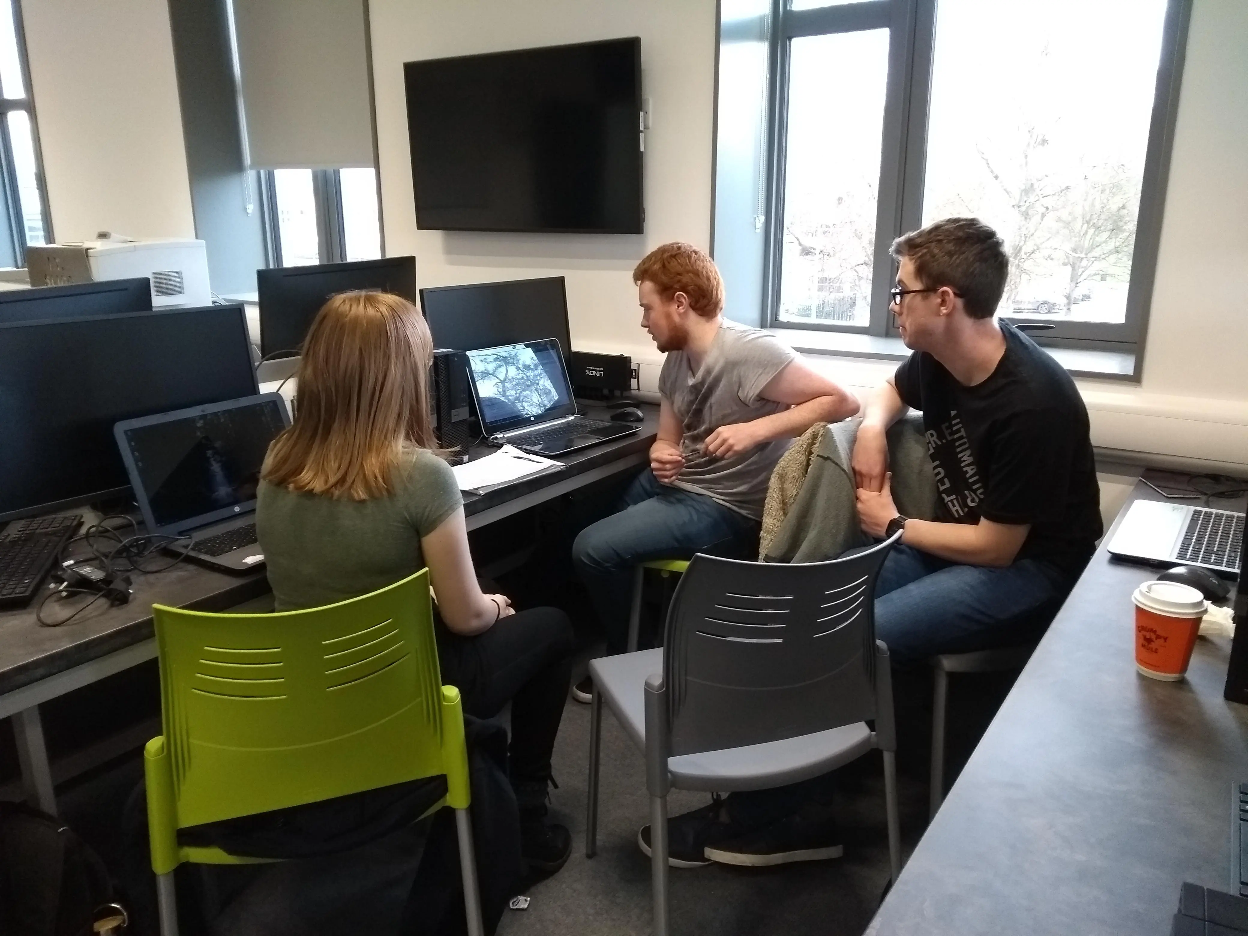 Three people in a computer lab looking at a laptop.